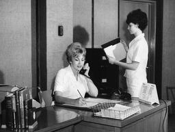 Student answering phone in office setting, ca. 1966