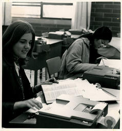 Students at typing machines, looking at books