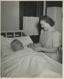 Nurse attending to elderly person in hospital bed