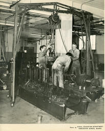 Students attach chains to a piece of machinery, ca. 1960