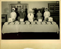 Five people posing in front of a display of decorated cakes