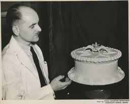 Person looks at cake, ca. 1951