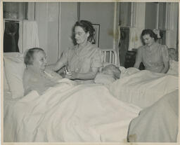 Elderly patients in hospital beds being helped by nurses
