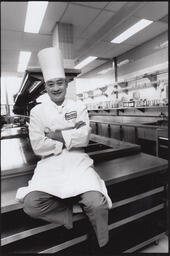 Student chef sitting on a counter in an empty kitchen classroom