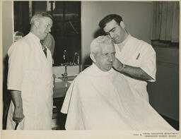 Barbering student and teacher giving customer a haircut, ca. 1954