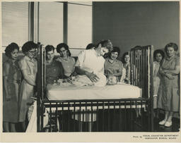 Nursing instructor shows class baby doll in crib, ca. 1960