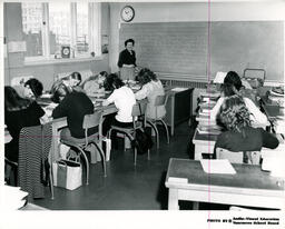 Students at desks in classroom with instructor at blackboard, ca. 1972