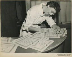 Instructor signing certificates at a desk, ca. 1954