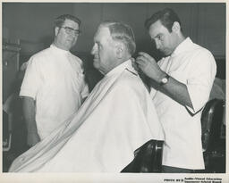Customer getting a haircut from barbering student and instructor, ca. 1972