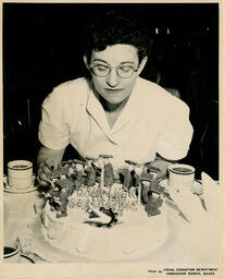 Person leaning over cake that says "Good luck to the Graduating Class," ca. 1954