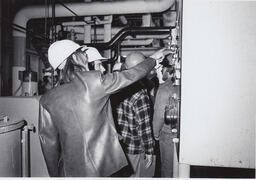 Two students in an industrial building looking closely at a machine