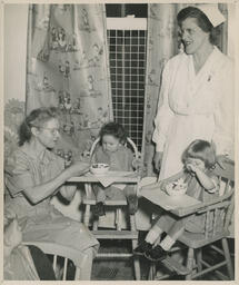 Two toddlers in high chairs being fed by nurses