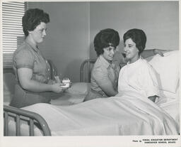 Two student nurses help patient sit up in hospital bed, ca. 1963