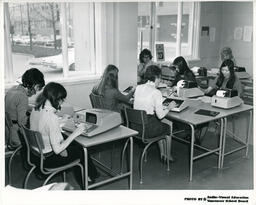 Eight students at desks using calculating machines