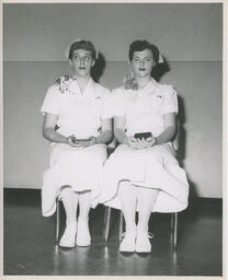 Two nursing students sitting and holding diplomas