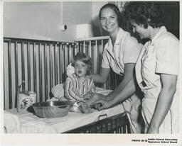 Practical Nursing students attending to toddler in crib, ca. 1972