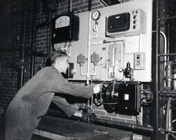 Student working at a wall of electronic devices, ca. 1962