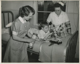 Nurses attend to a child with a broken leg who is lying on bed playing with toys