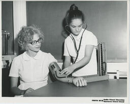 Nursing student taking blood pressure of another student, ca. 1972