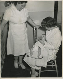 Nurse gives a bottle to baby on lap while instructor observes