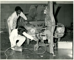 Two auto students working on a car with hood open
