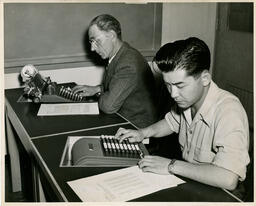 Two people working on specialized calculator typewriters, ca. 1950