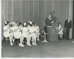 Administrator at podium speaks while nurses clap