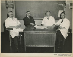 Group of barbering instructors sitting at a desk, ca. 1955
