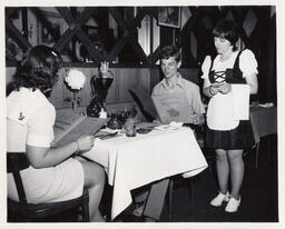 Server waits on customer with menu, ca. 1972
