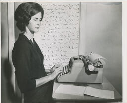 Person typing with shorthand chart on wall behind them