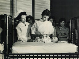 Nursing students with baby doll in crib, ca. 1960