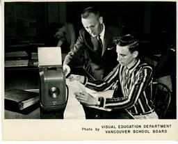 Instructor and student looking over punch clock paper, ca. 1959