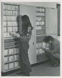 Two students standing at a cabinet of tapes
