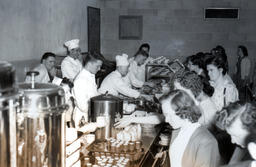 Customers line up at a cafeteria setting with chefs serving them