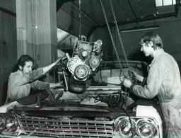 Two auto students lowering an engine into a car, ca. 1972