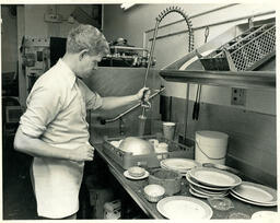 A student rinses dishes in an industrial sink