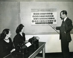 Instructor pointing to poster of typewriter keyboard, ca. 1950
