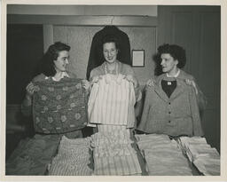 Three sewing students holding up garments