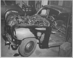Car in body shop with engine exposed, ca. 1950