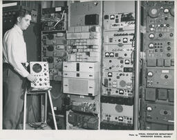 Student with a oscilloscope beside wall of communications equipment, ca. 1966
