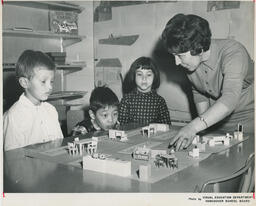 Student in Family Aide program and three children looking at dollhouse furniture