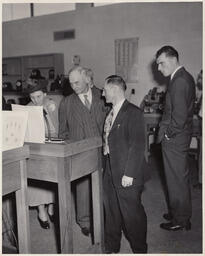 Instructors looking at a paper on a podium, ca. 1949