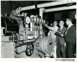 Instructor and guests observe steam engine, ca. 1972
