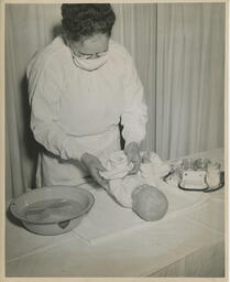 Student nurse wearing with a baby doll and wash bin on table