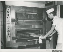 Baking student takes pies out of an oven, ca. 1972