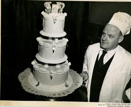 Instructor looks at a three-layer cake, ca. 1951