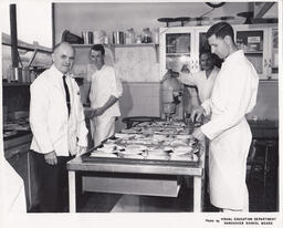 Instructor and three students preparing pie slices on plates on a table, ca. 1963