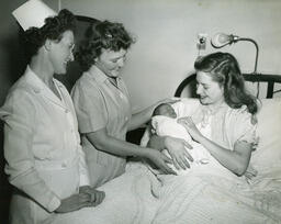 New mother holds newborn as nurses look on