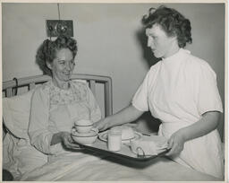 Nurse serves a meal to a smiling patient in hospital bed