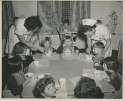 Children eating at a round table with nurses helping them